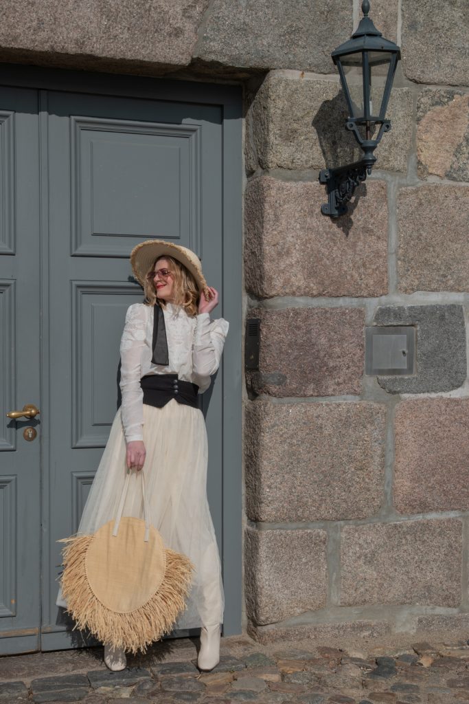 Eine Frau in einem weißen Kleid und Hut hält eine Tasche in der Hand.